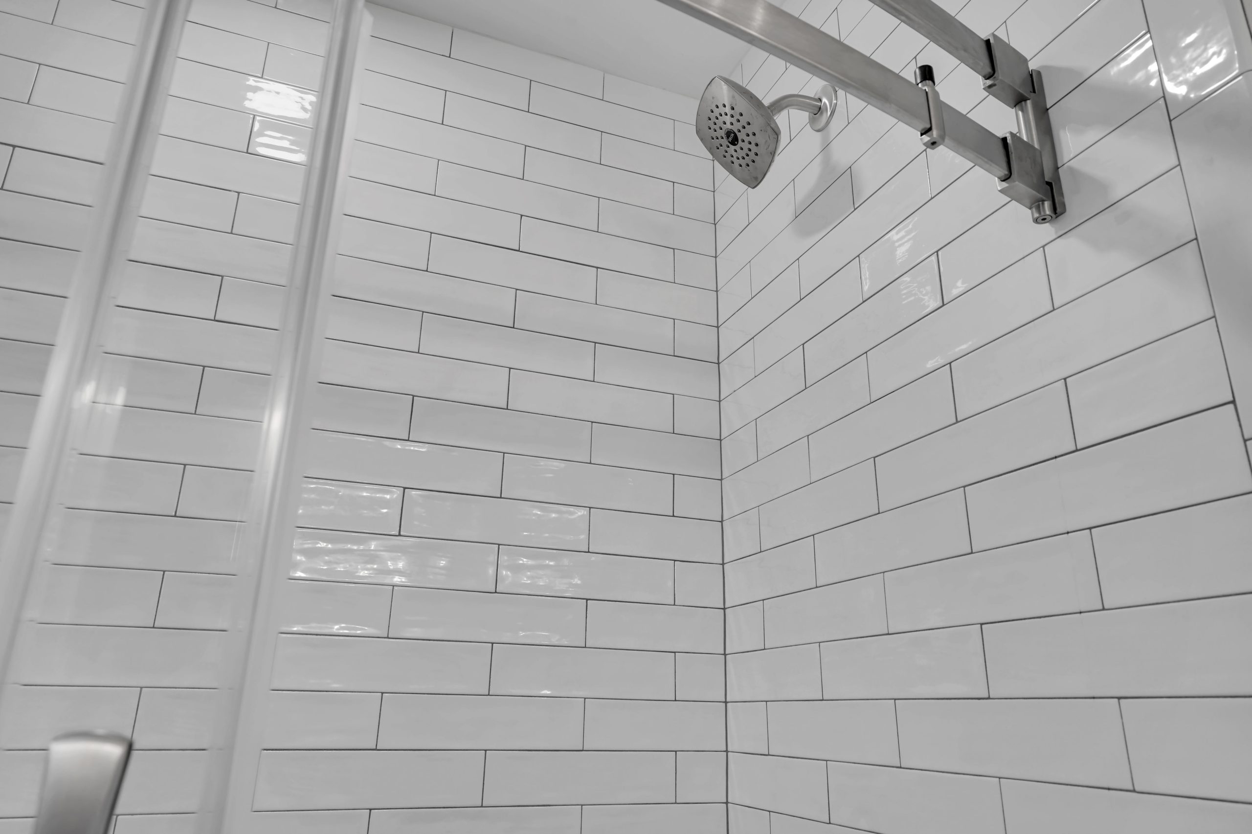 A shower with white subway tile walls, a silver showerhead, and glass shower doors. The tiles are arranged in a staggered pattern, and the overall appearance is clean and modern.