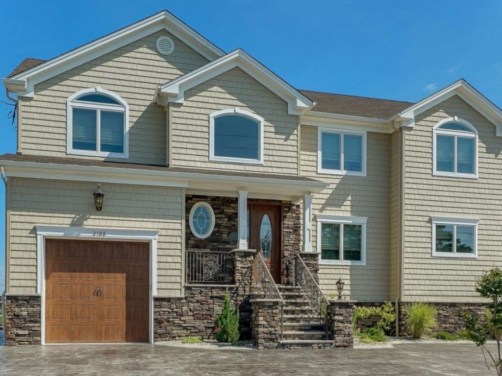 Two-story home with beige siding, stone accents, and white trim featuring a wooden front door and garage, representing the importance of choosing the right contractor for quality home construction.