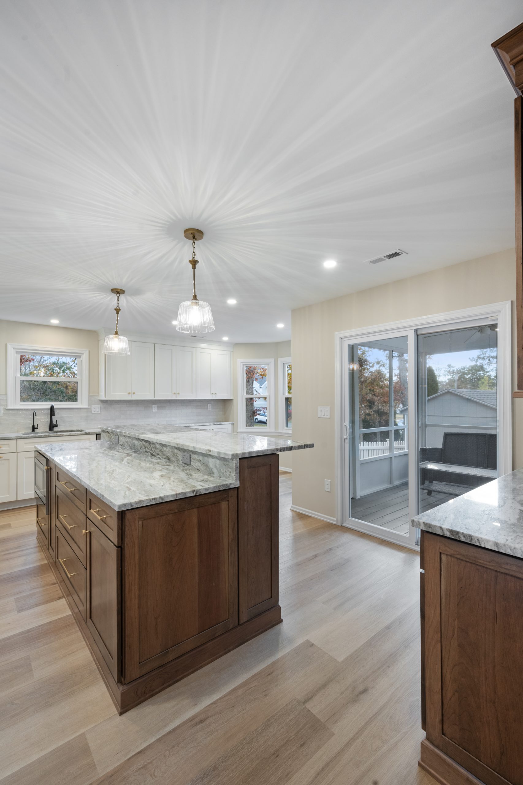 Spacious modern kitchen with white cabinets, a large marble island with wood base, pendant lights, wood flooring, and sliding glass doors leading to a patio.