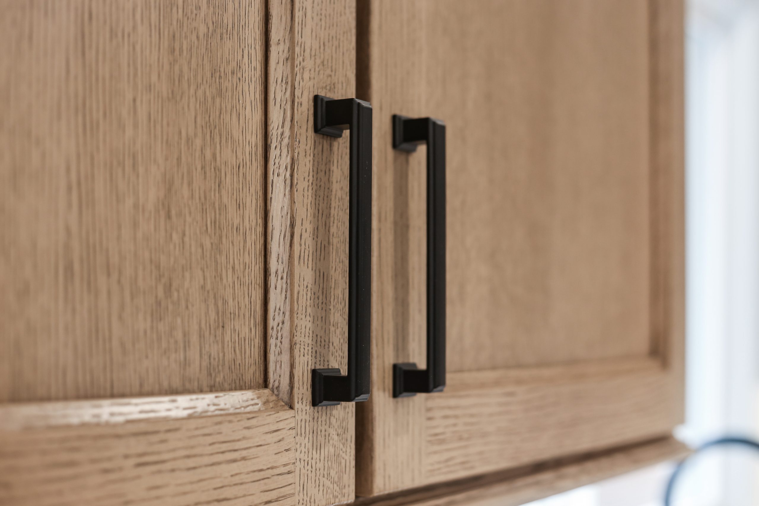 Close-up of two light wood cabinet doors with modern black metal handles, showing the wood grain and simple design.