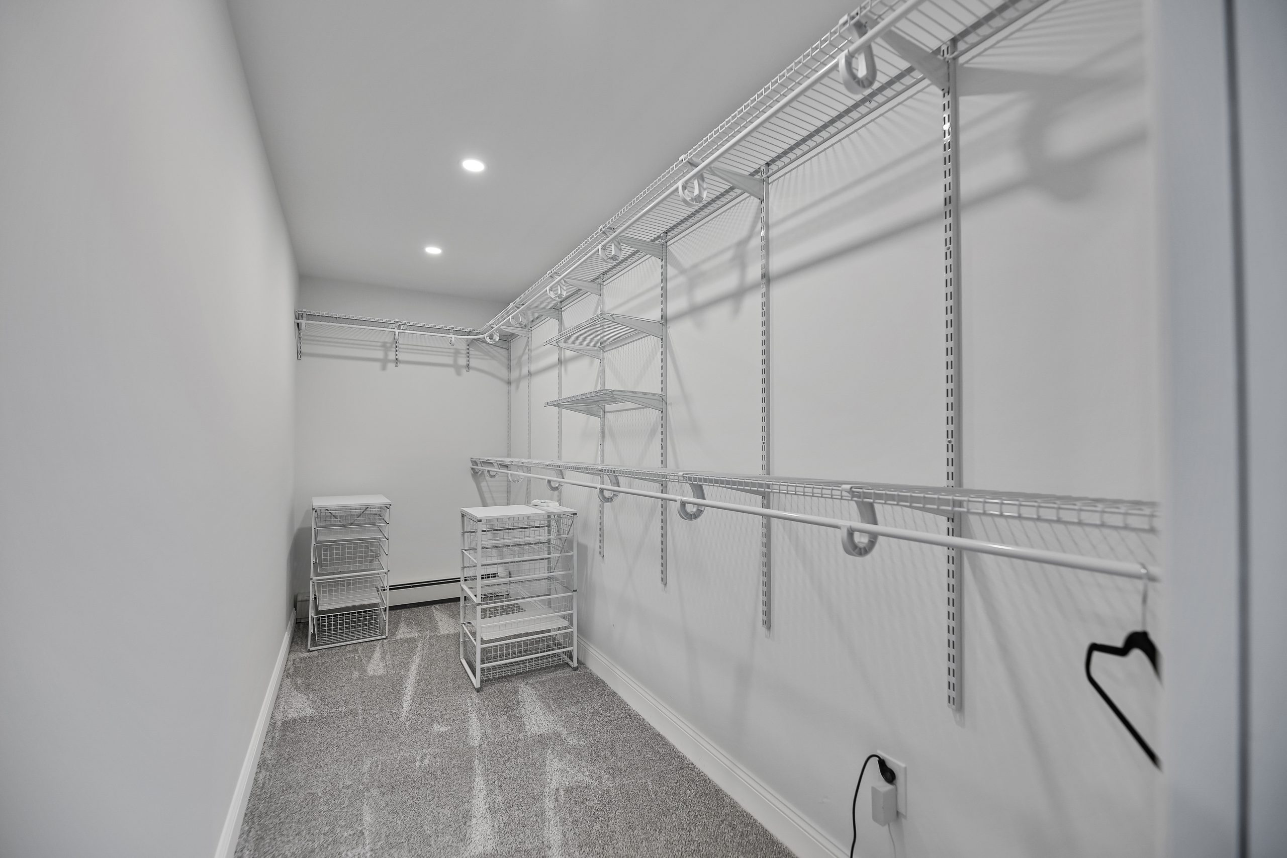 A spacious, modern walk-in closet with white wire shelving and drawers on both sides, white walls, recessed ceiling lights, and a glossy gray floor. The closet is empty except for a single black hanger.
